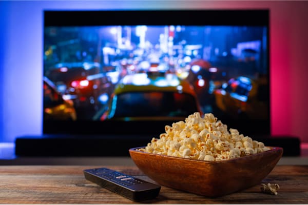 A bowl of popcorn and a remote control in front of a television displaying a city street scene.